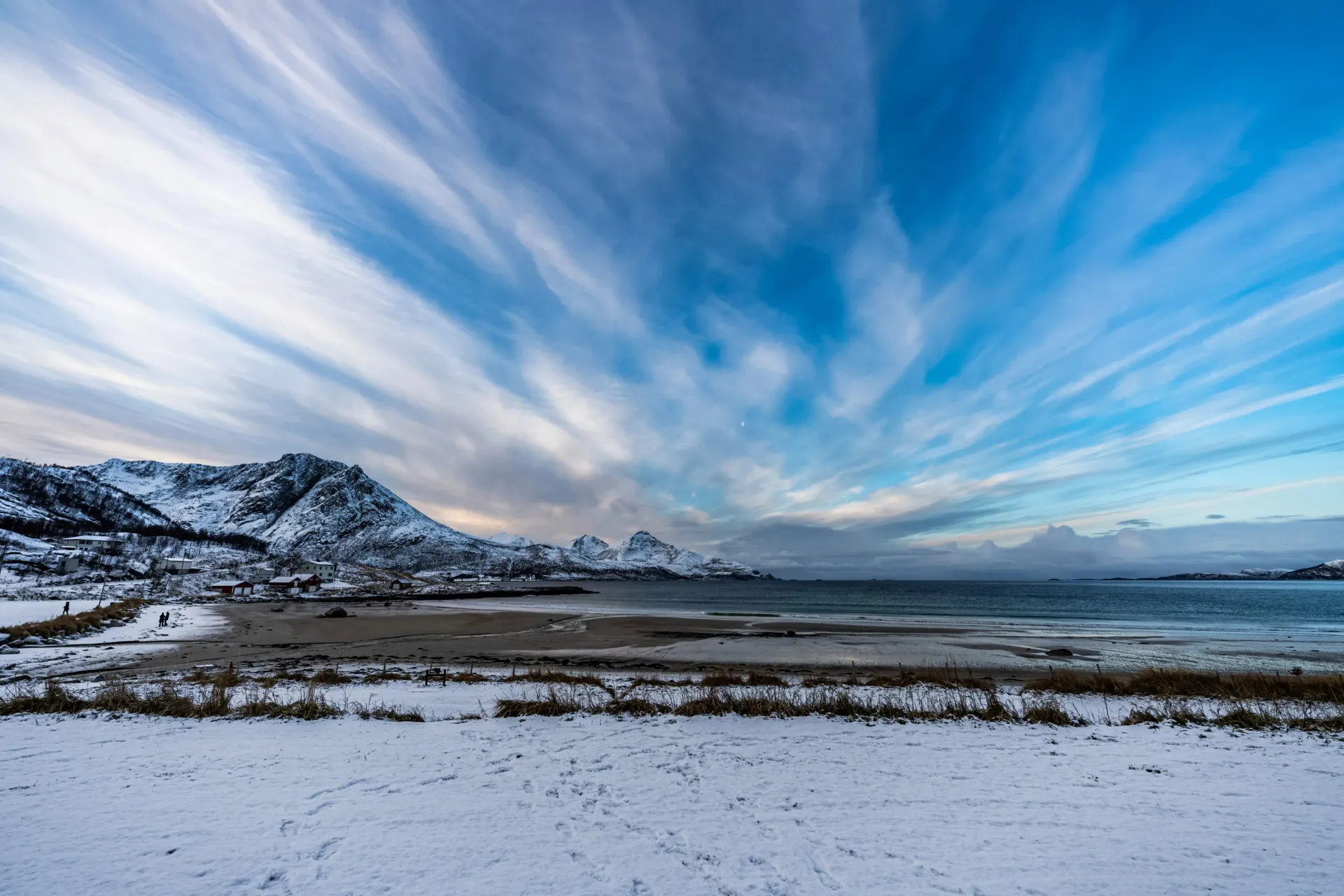 Panoramic view of a serene coastal Arctic fjord surrounded by snow-dusted mountain slopes in Northern Norway