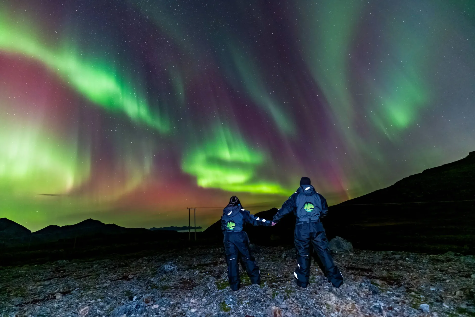 Travelers observing an expansive green auroral arch stretching across the dark night sky in Northern Norway