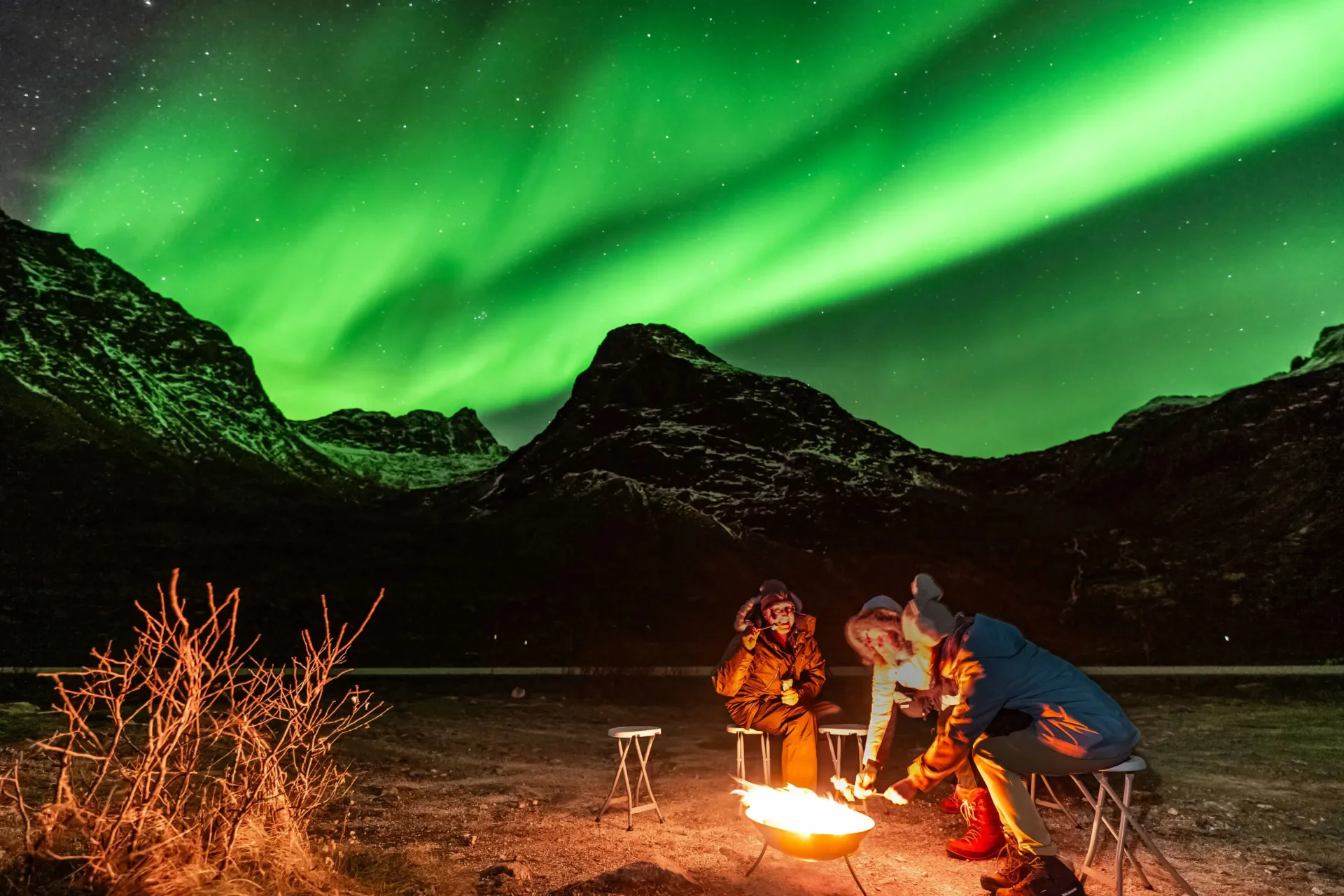 Couple standing outdoors holding hands under a glowing green Northern Lights canopy in Tromsø Norway