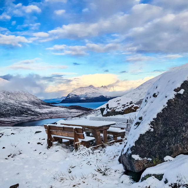 Snowy mountain fjord landscape with a wooden picnic table during a daytime coastal sightseeing excursion in Tromsø