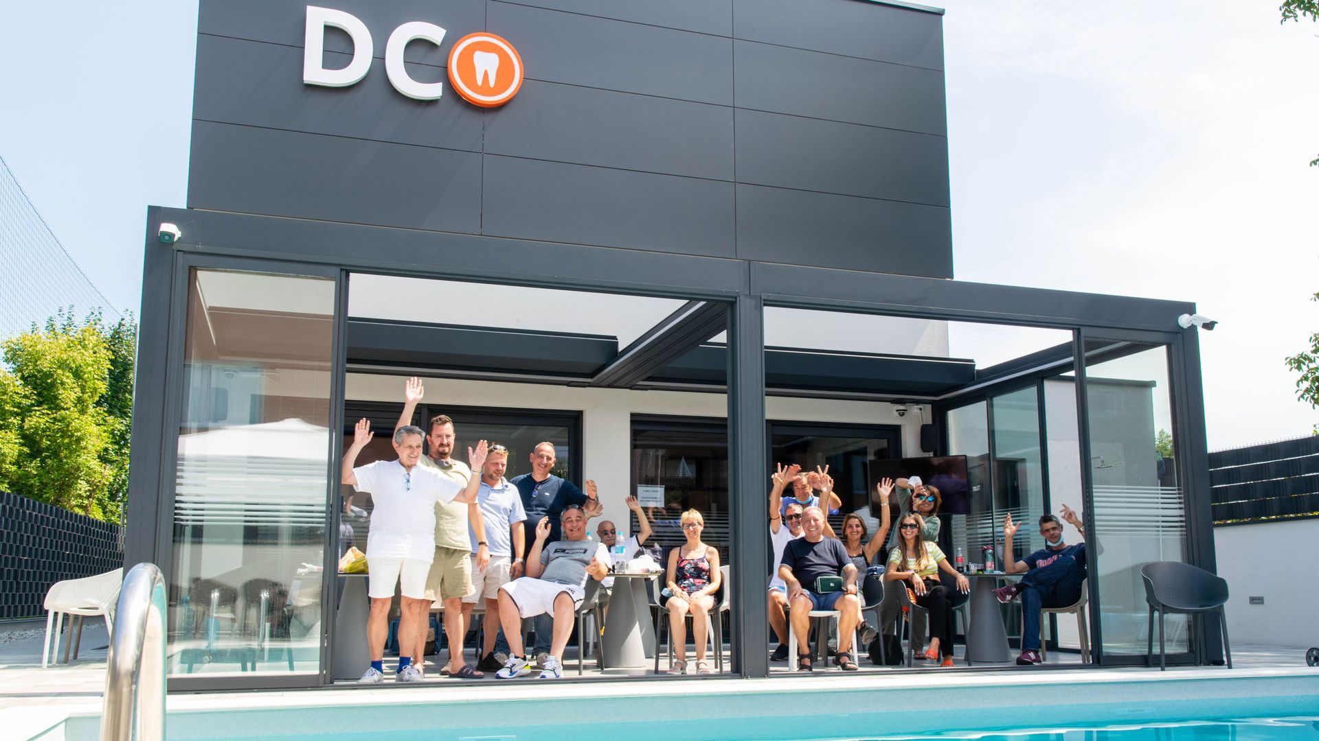 Un gruppo di persone si trova davanti a un edificio accanto a una piscina. Studio dentistico ostojic