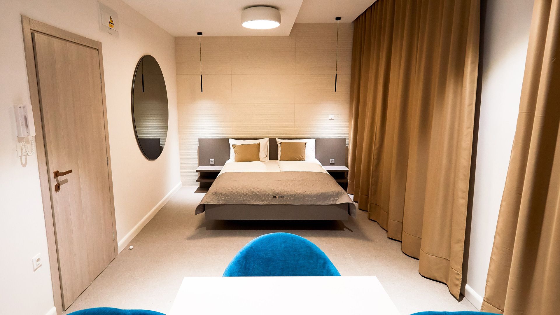 Camera da letto minimalista con letto, specchio rotondo e tende beige.