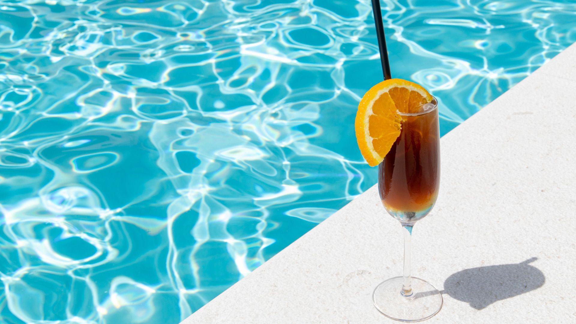 Un bicchiere di vino con una cannuccia e una fetta arancia accanto a una piscina.