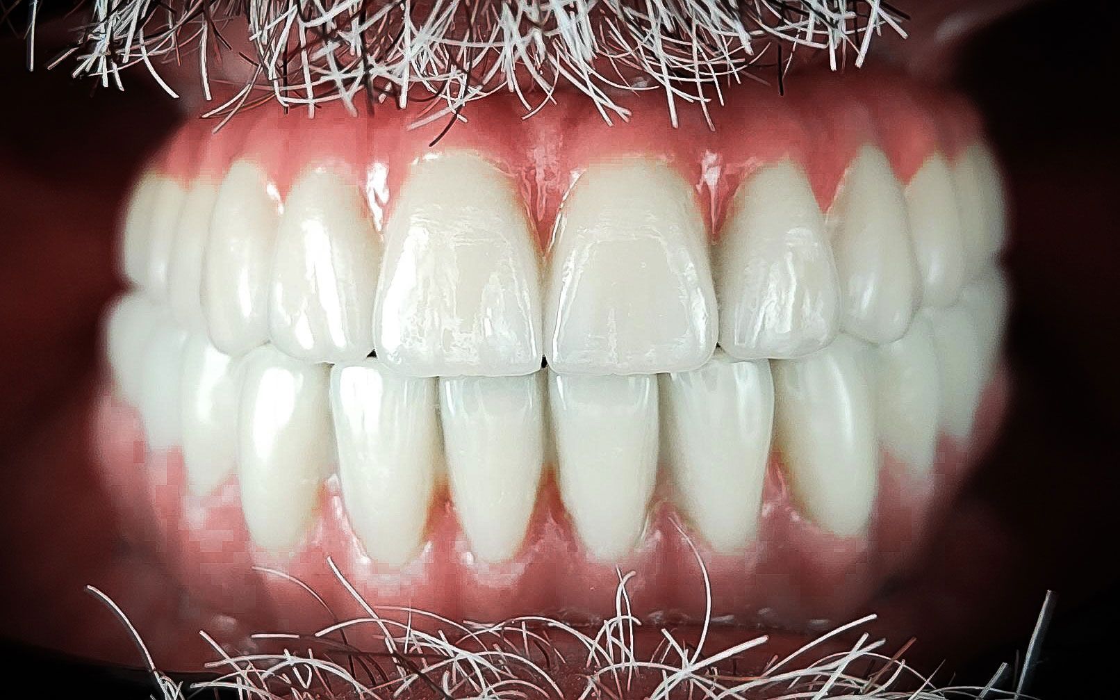 Primo piano di una bocca sorridente con denti bianchi e gengive rosse, incorniciata da ciocche di capelli o pelliccia di un bianco ghiaccio.