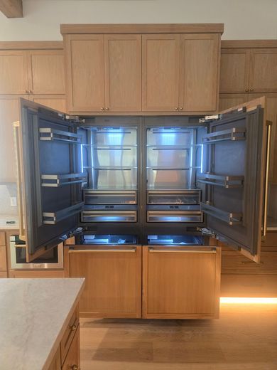 Open built-in wall cabinet with shelves and drawers in a kitchen, wood finish and glass shelves.