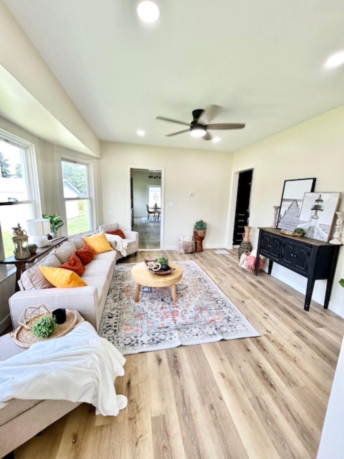 Living room with light wood floors, a beige sectional sofa with orange and yellow pillows, and a black cabinet.