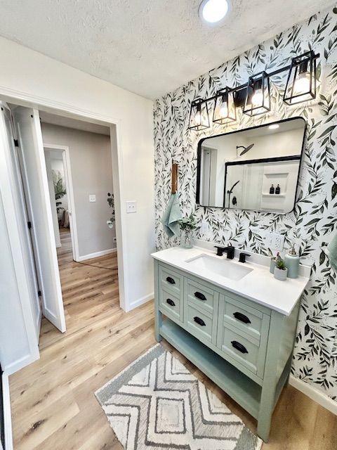 Bathroom with green vanity, patterned wallpaper, black mirror and light fixture.