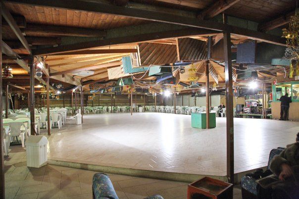 Una pista da ballo al coperto, sotto un tetto con travi in ​​legno, circondata da tavoli, sedie e decorazioni sospese.