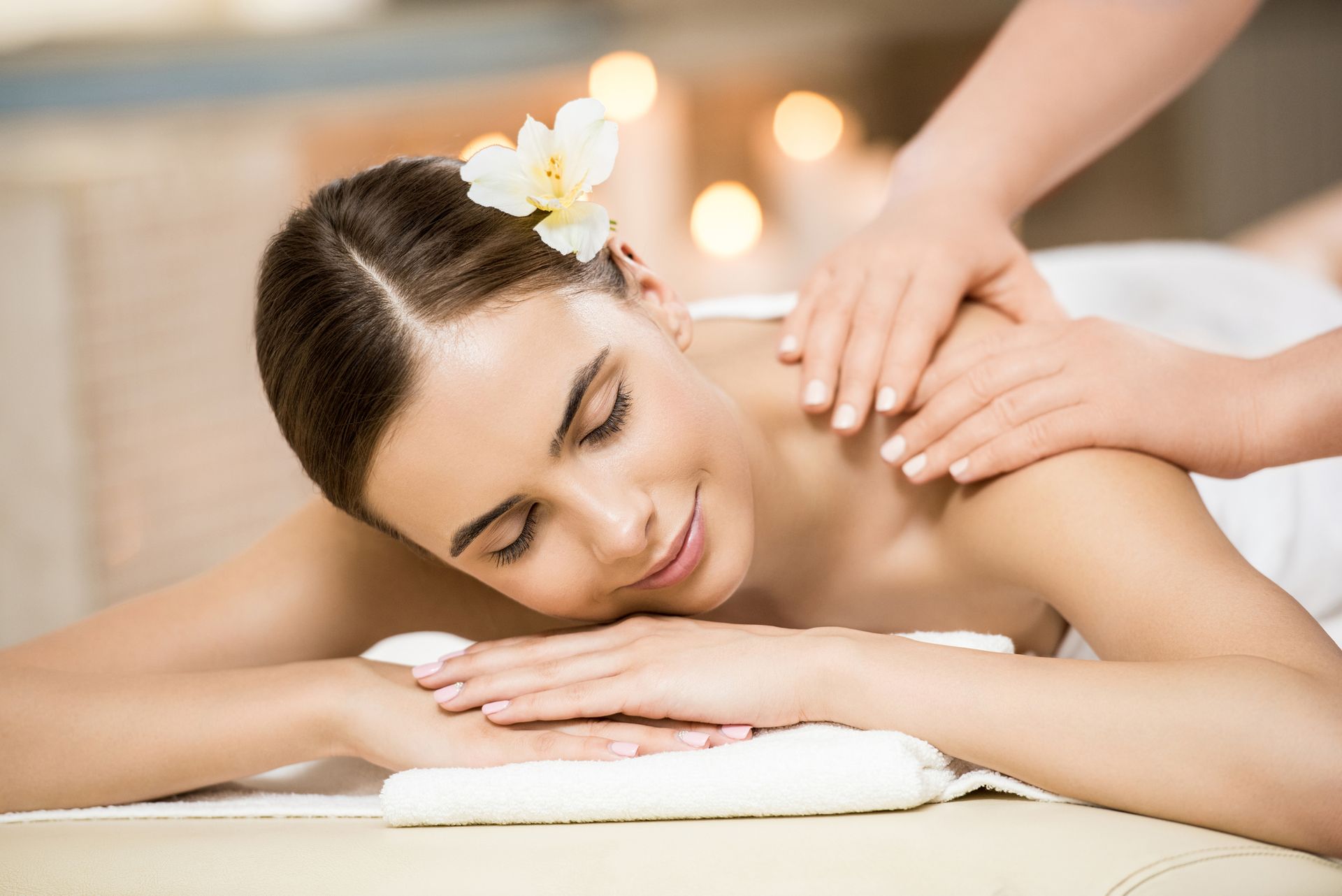 Una persona con un fiore tra i capelli si rilassa su un lettino da massaggio mentre riceve un massaggio alle spalle in una spa.