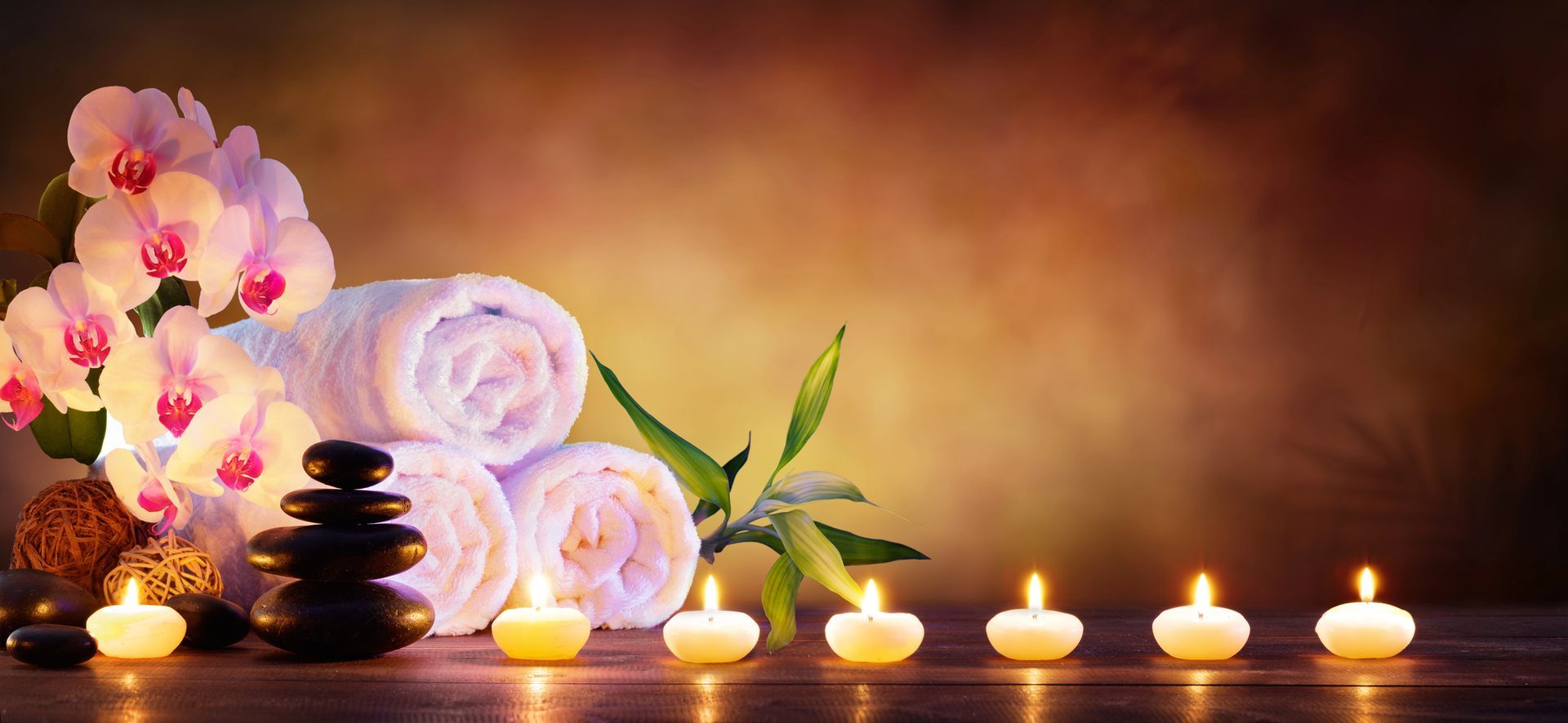 Un'atmosfera da spa con asciugamani bianchi piegati, orchidee, una pila di pietre nere, bambù e una fila di candele profumate.