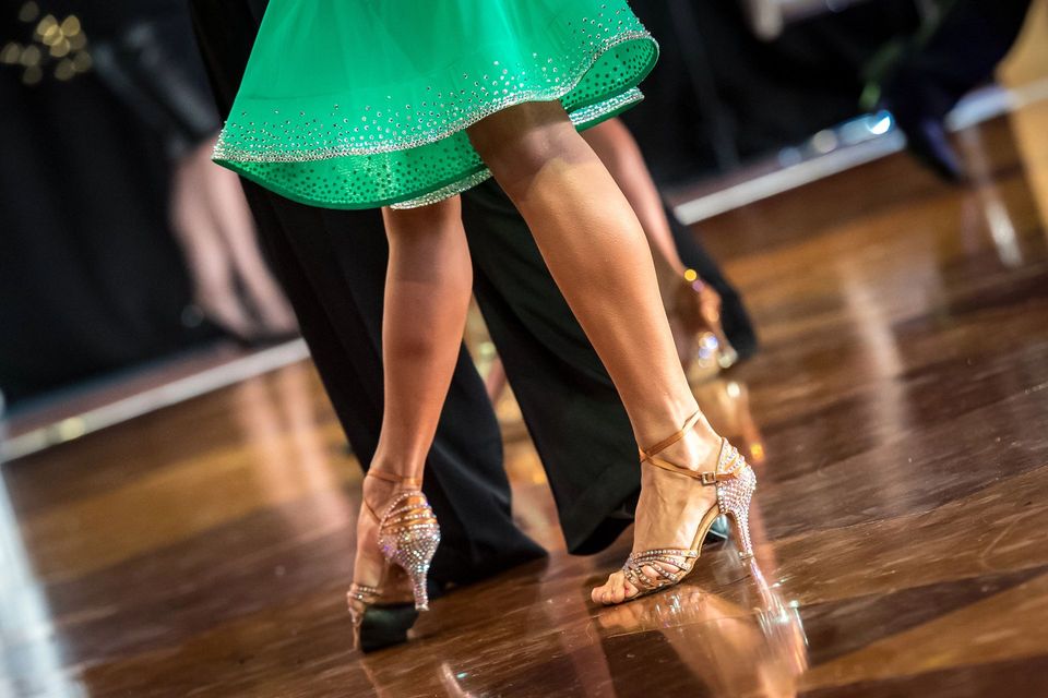 Ballerini in abiti eleganti e scarpe scintillanti si esibiscono su una pista da ballo in legno.