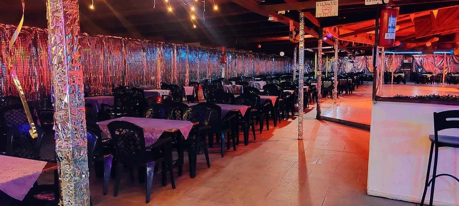 File di tavoli con tovaglie viola e sedie nere sotto un tendone dai toni rossi, illuminato da una luce soffusa e decorato a festa.
