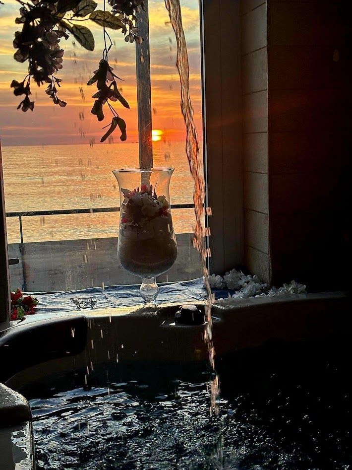 Un tramonto sull'oceano da una stanza in penombra con una vasca idromassaggio e una cascata.