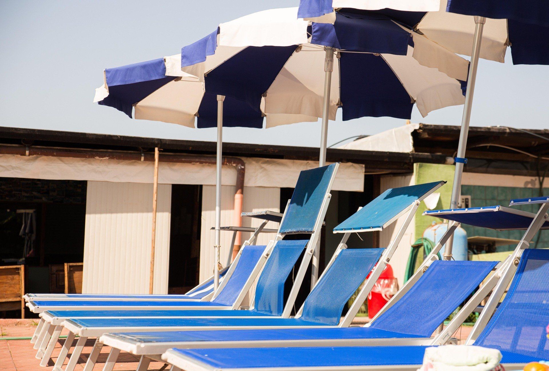 In un resort all'aperto, lettini blu sono allineati in fila sotto ombrelloni a righe blu e bianche.