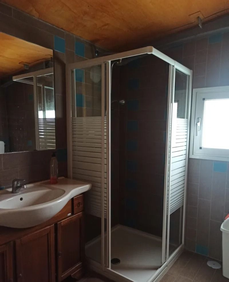 Un bagno con mobiletto in legno, lavabo bianco e box doccia angolare bianco con pannelli satinati su pareti scure.