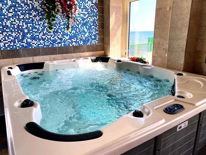 Una vasca idromassaggio quadrata con acqua gorgogliante, incastonata in una stanza con piastrelle a mosaico blu e una finestra che si affaccia sul mare.