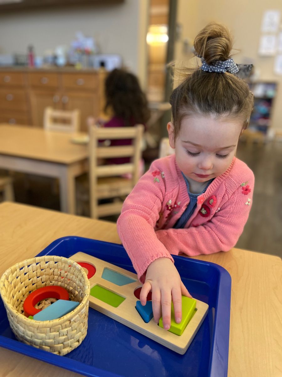 A little girl is playing with a wooden puzzle on a table.