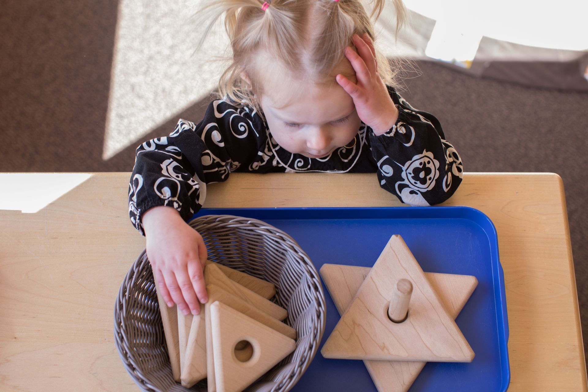 Child at a table working with wooden stacking toys in a blue tray