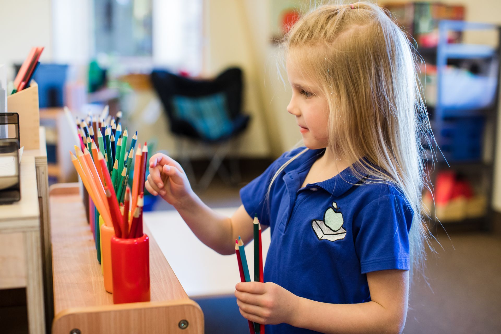 Child in a blue shirt picking colored pencils in a classroom art area
