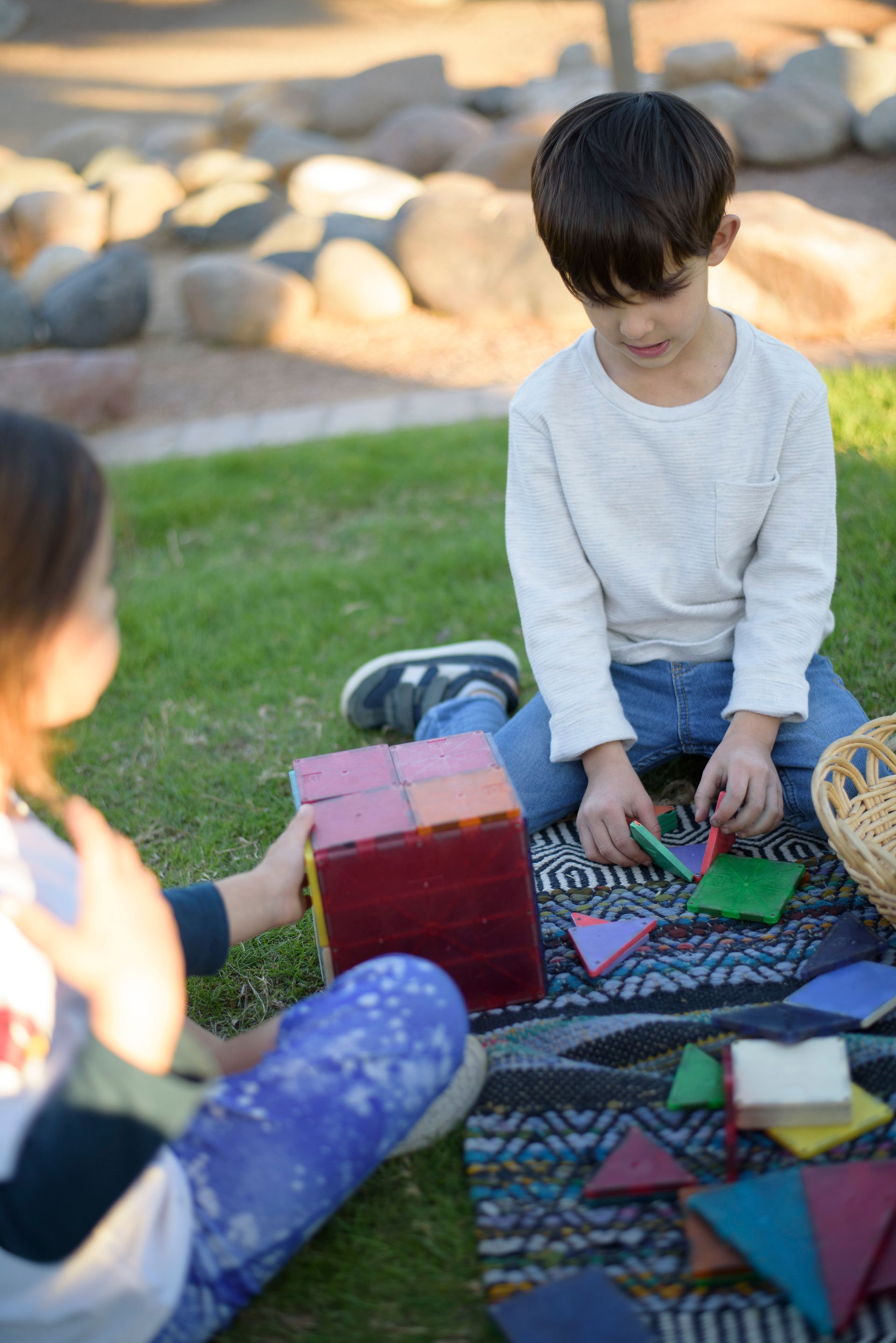 Children playing with colorful blocks on a blanket outdoors in sunlight