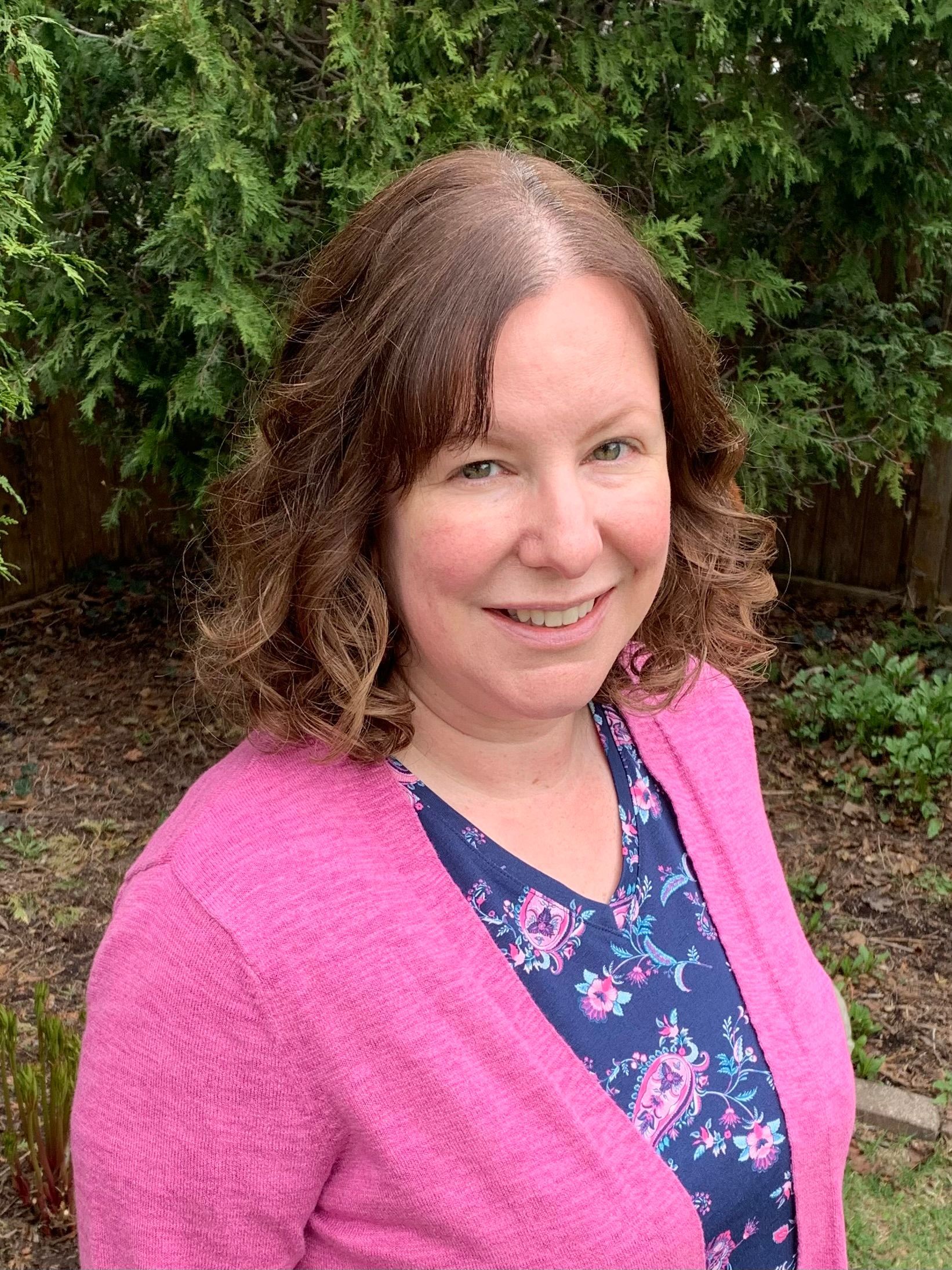 A woman in a pink sweater and floral shirt is smiling for the camera.