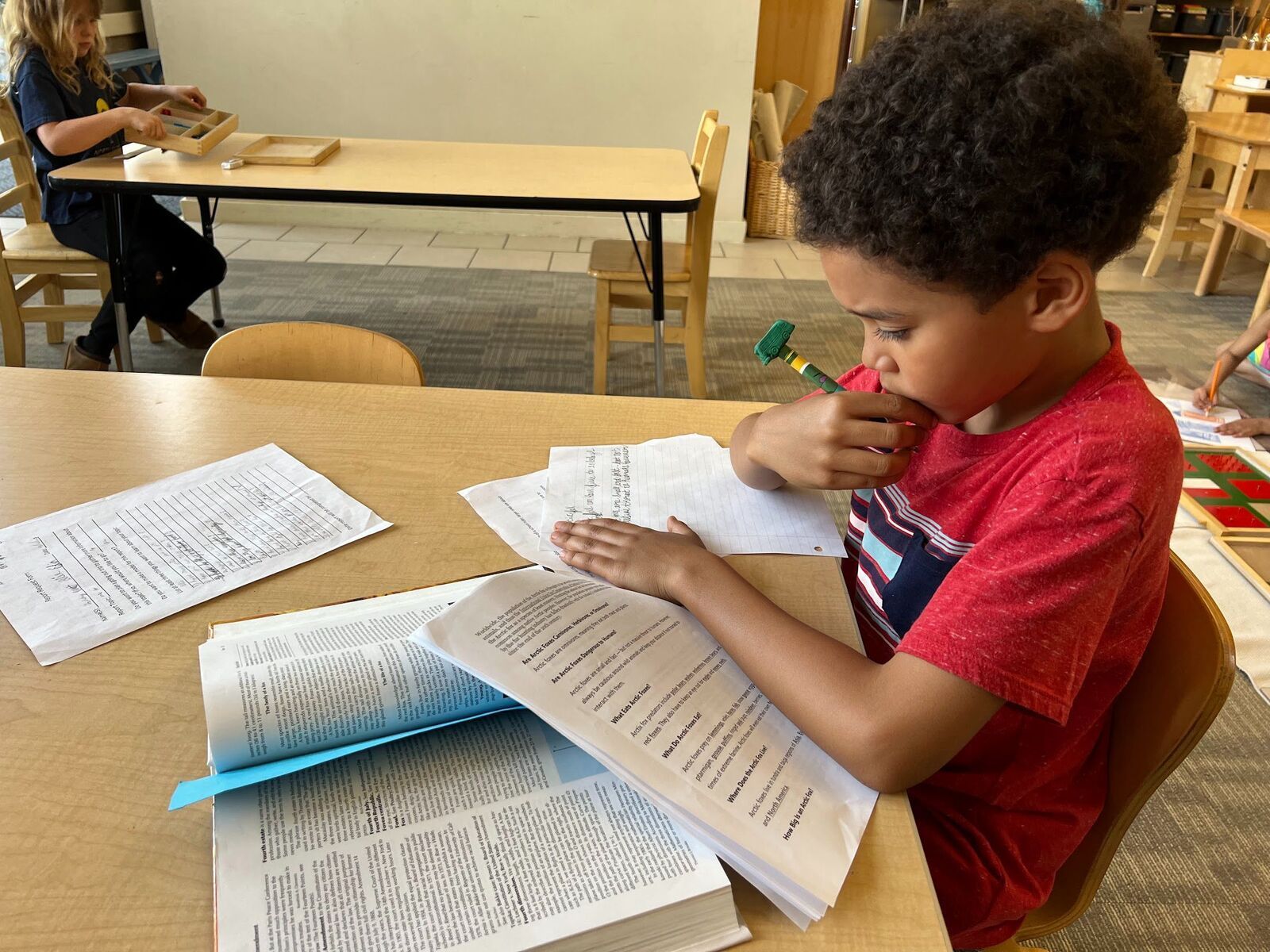 A young boy is sitting at a table reading .ant taking note