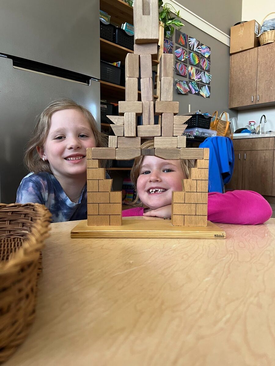 Two young girls are sitting at a table playing with wooden blocks.