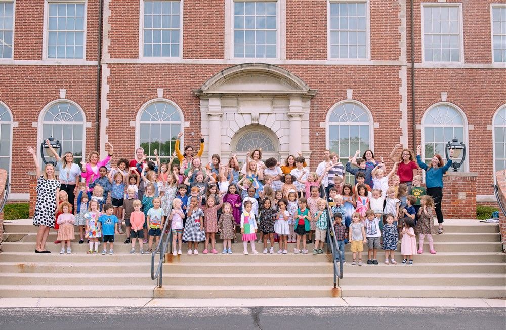 A large group of people are standing on the steps of a brick building.