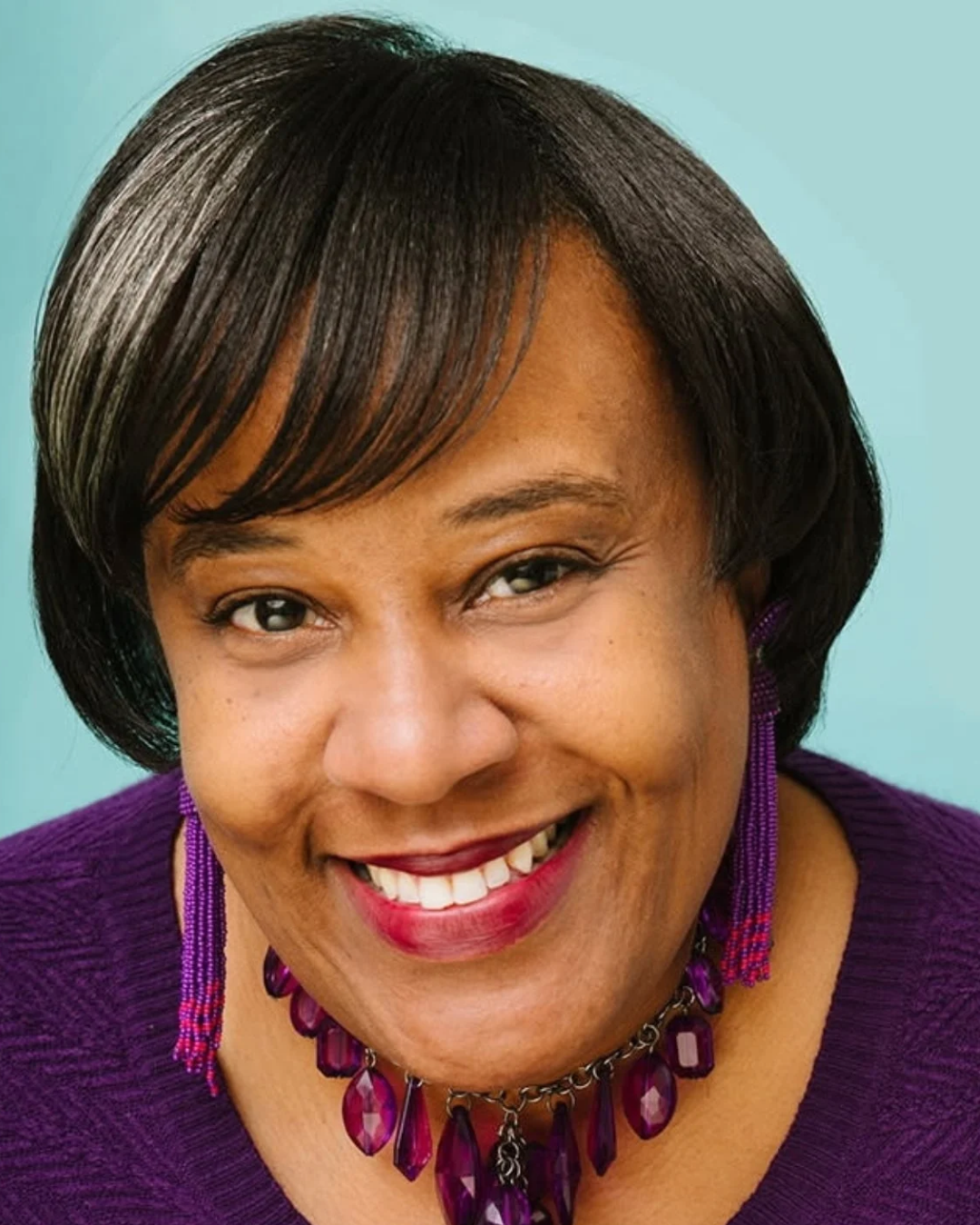 An older woman wearing a striped shirt and earrings smiles for the camera