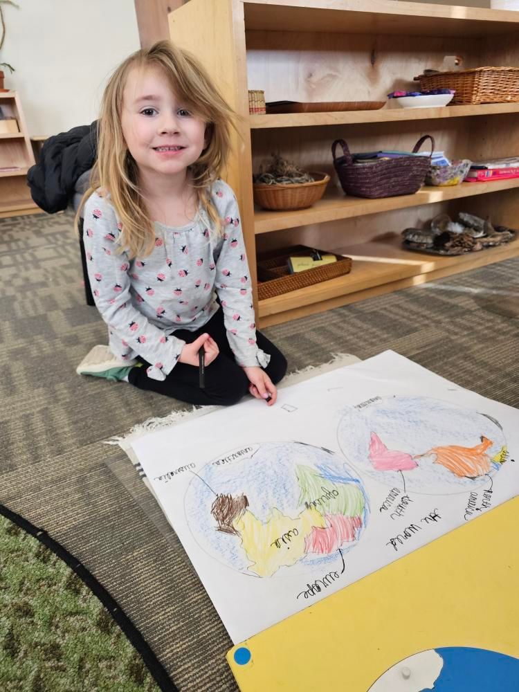 A little girl is sitting on the floor drawing on a piece of paper a world map montesori style