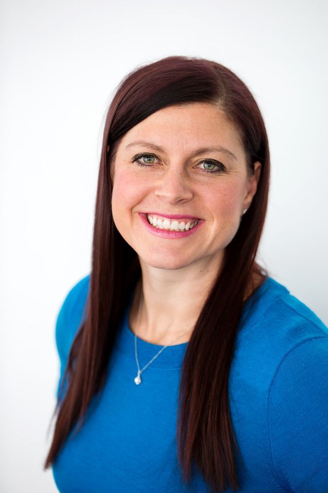 A woman with long red hair is wearing a blue shirt and smiling.