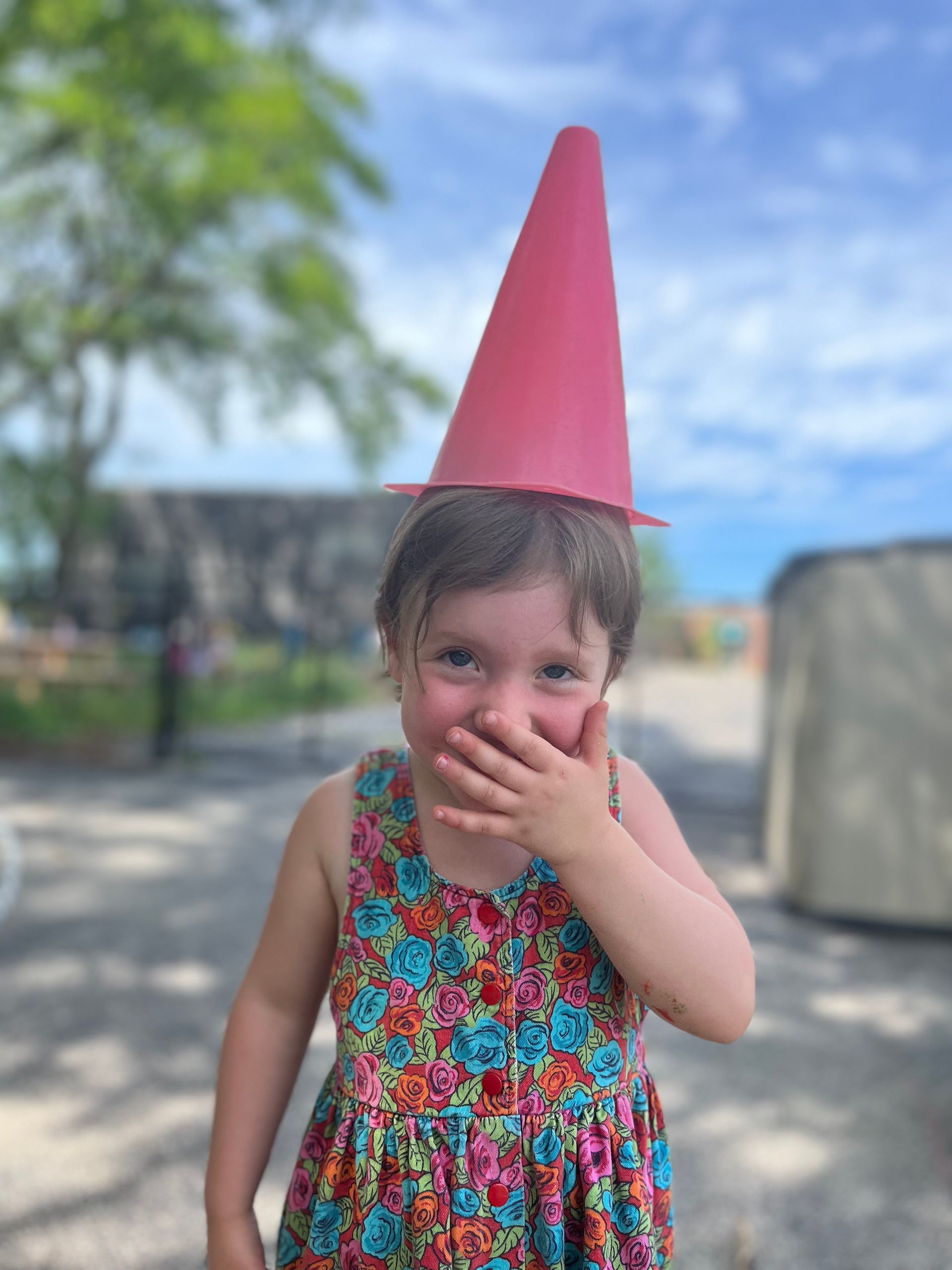 A little girl wearing a pink cone hat covering her mouth