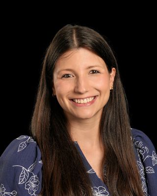 A woman in a black shirt is smiling with her arms crossed in front of a brick wall.