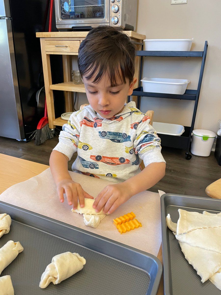 A young boy is sitting at a table making bread rolls.