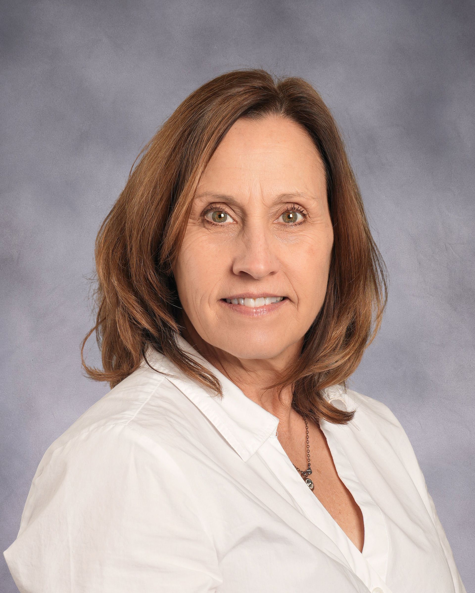 A woman in a grey sweater and white shirt is smiling for the camera.