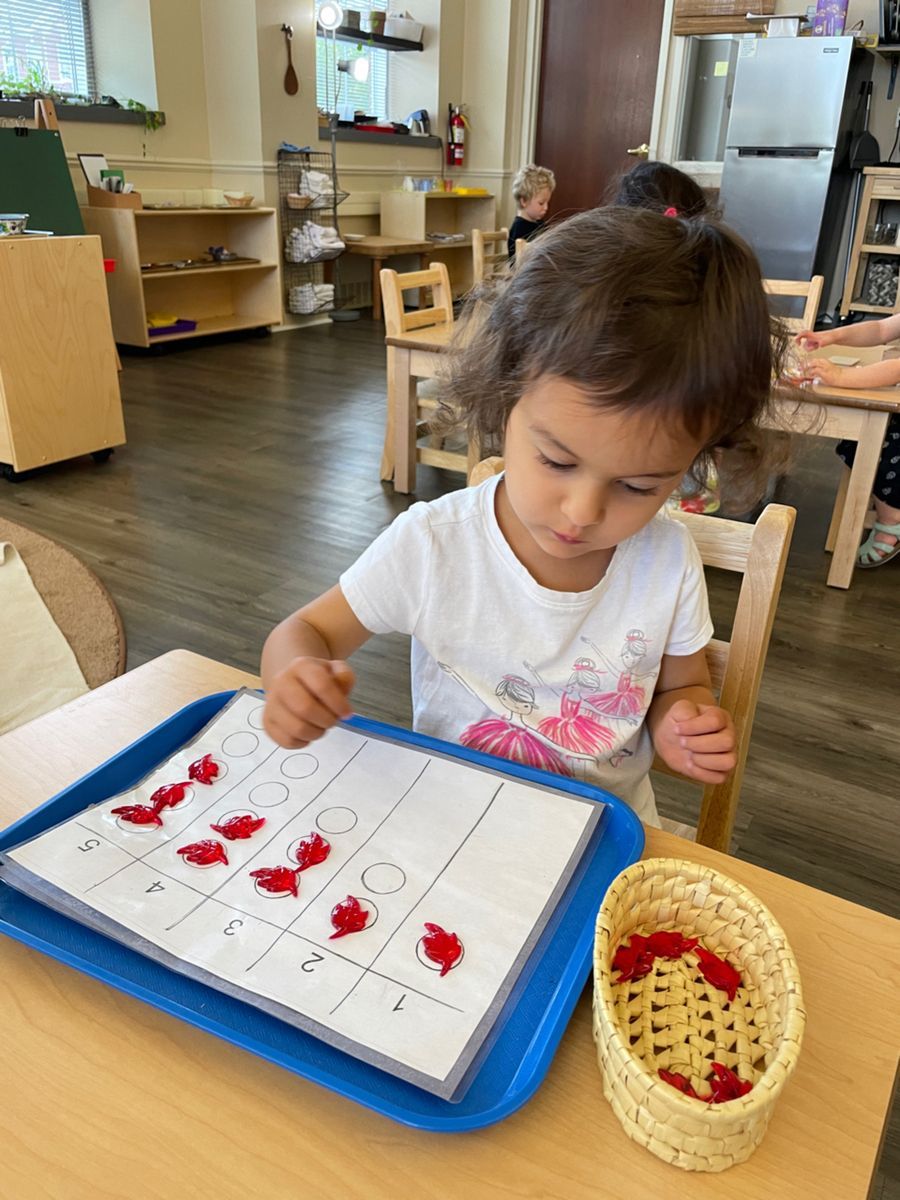 A little girl is sitting at a table working with montessori math materials