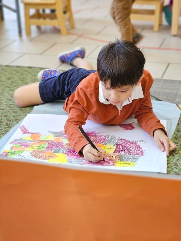 A young boy is laying on the floor painting a motessori map of the US on a piece of paper.