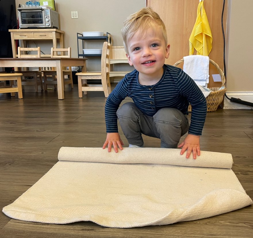 A young boy is kneeling down next to a roll of carpet.