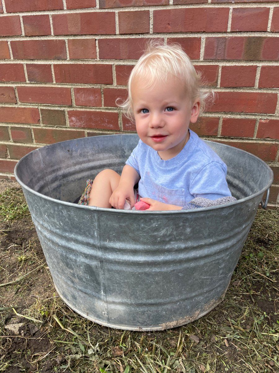A little boy is sitting in a metal tub in front of a brick wall.
