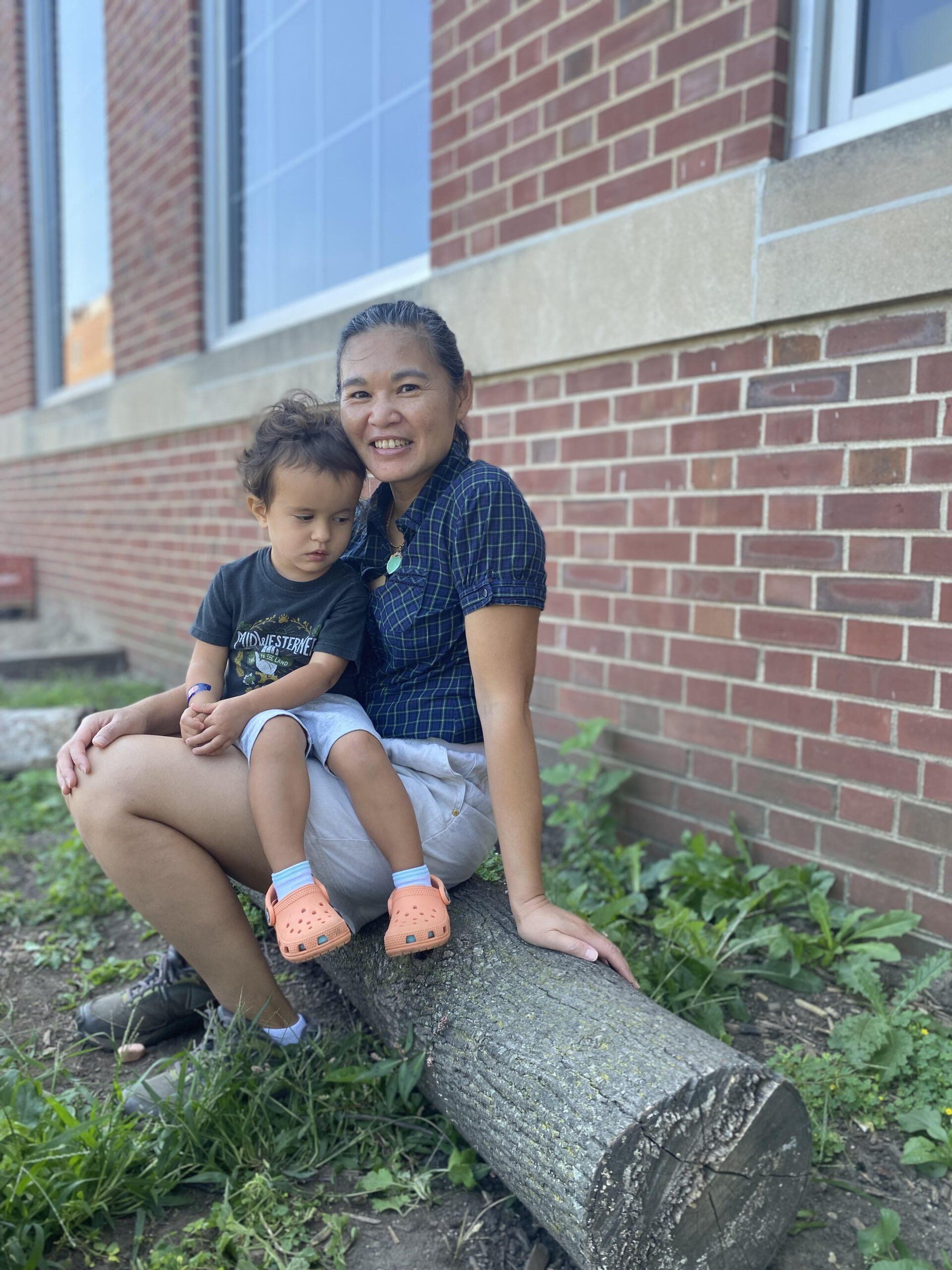 A woman is sitting on a log holding a baby.