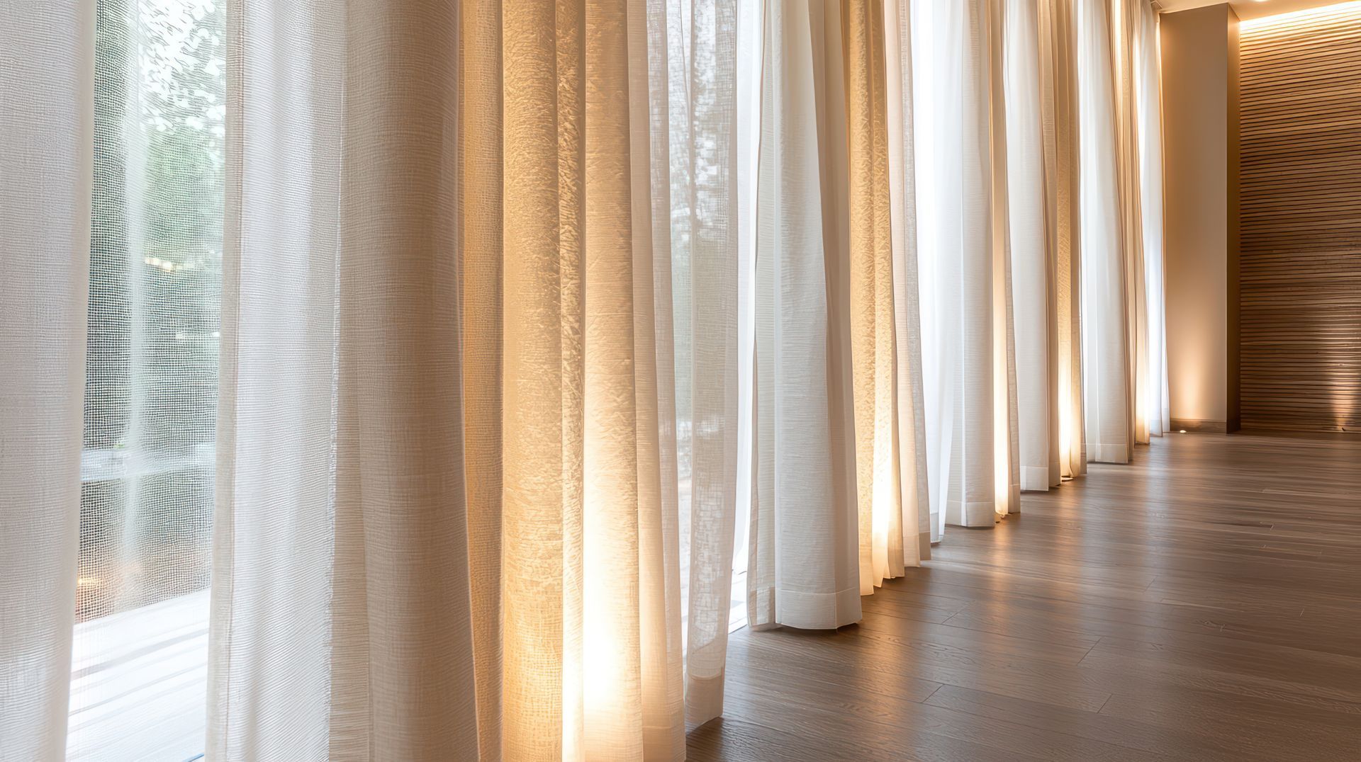 Sheer white curtains along a sunlit wooden hallway with warm light and a textured wall