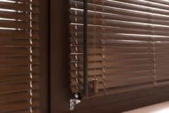 Closed brown window blinds with sunlight filtering through them