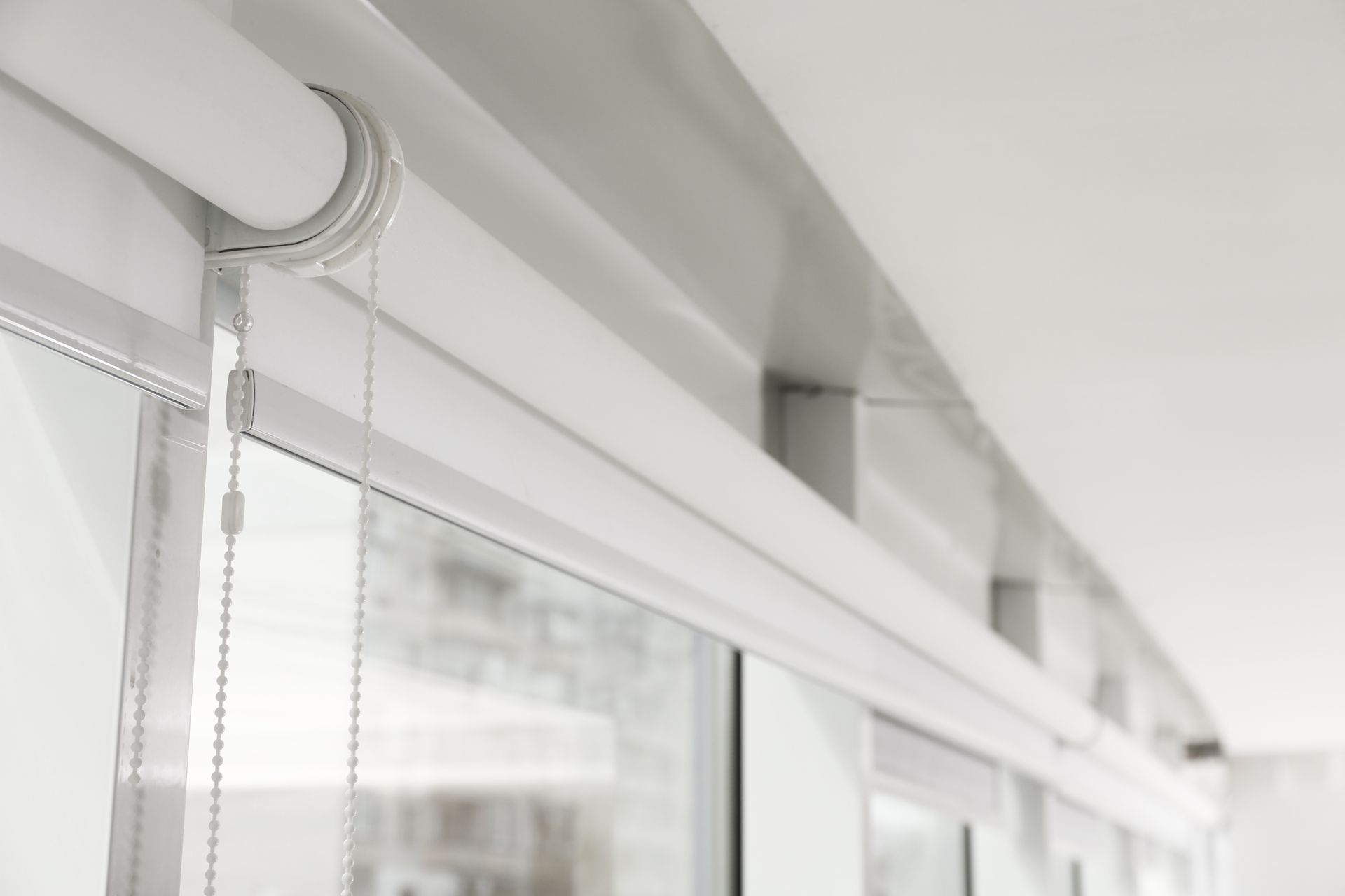 White roller blind with pull chains beside a window in a bright room