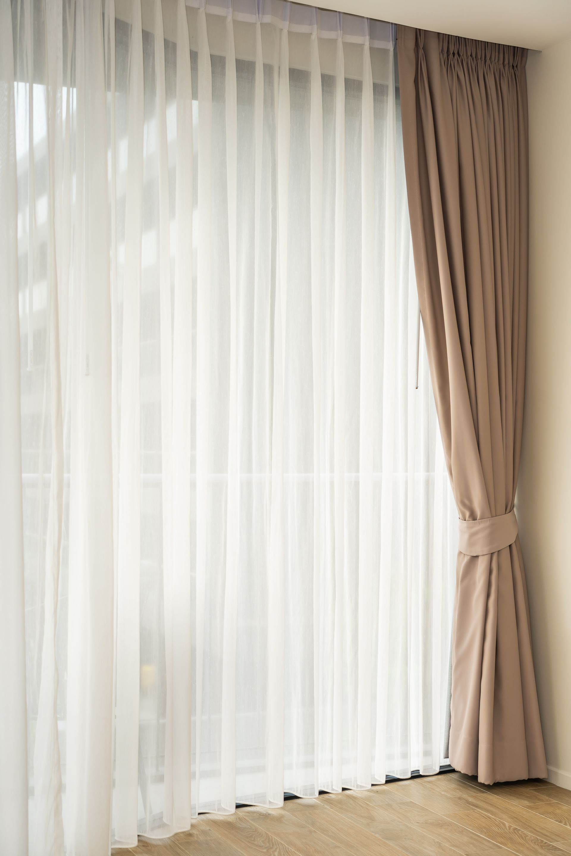 Sheer white curtains and beige drapes by a sunlit window in a bright room