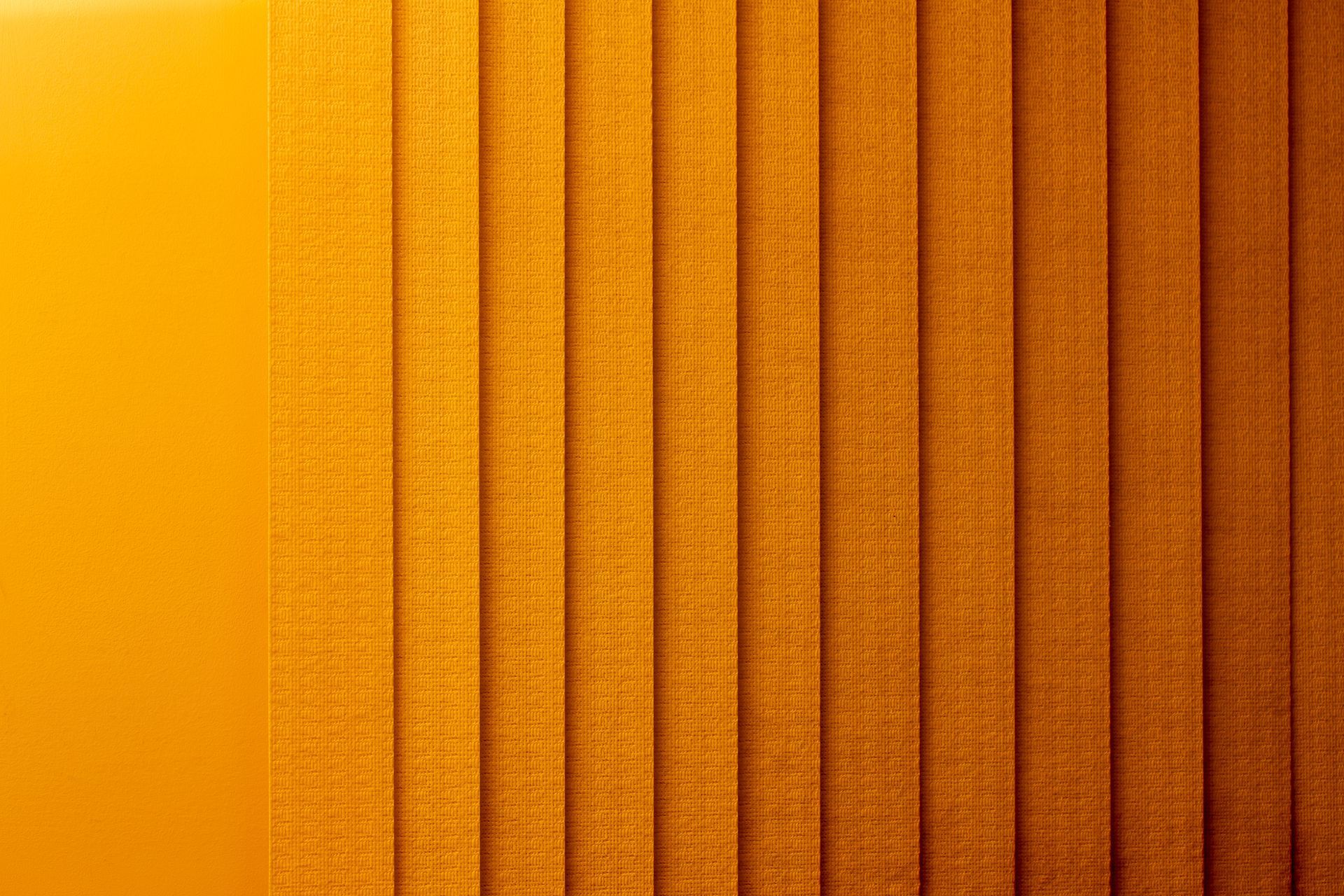 Orange textured vertical fabric stripes, like a close-up of a woven curtain or blind.