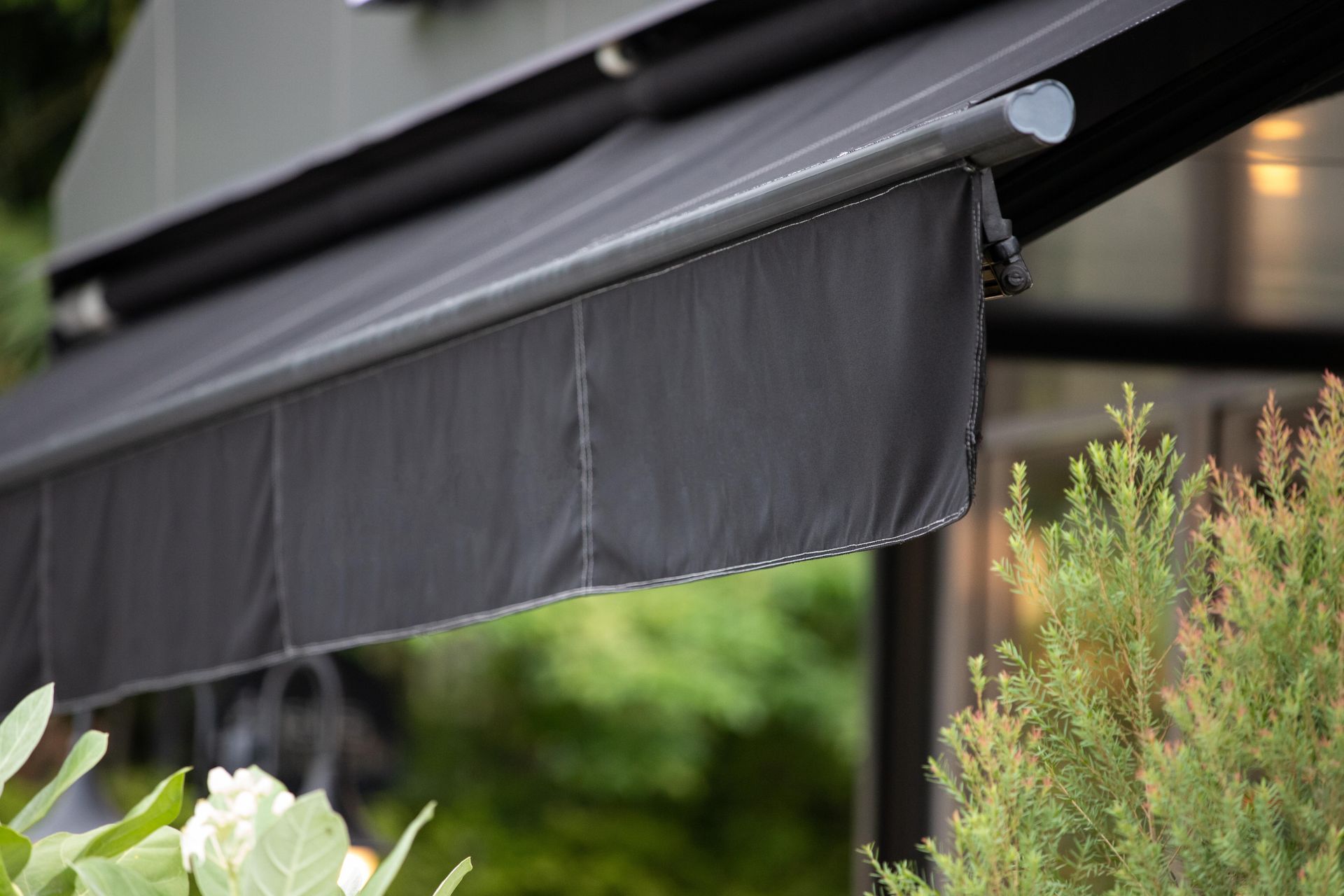 Black retractable awning over a garden with flowers and greenery