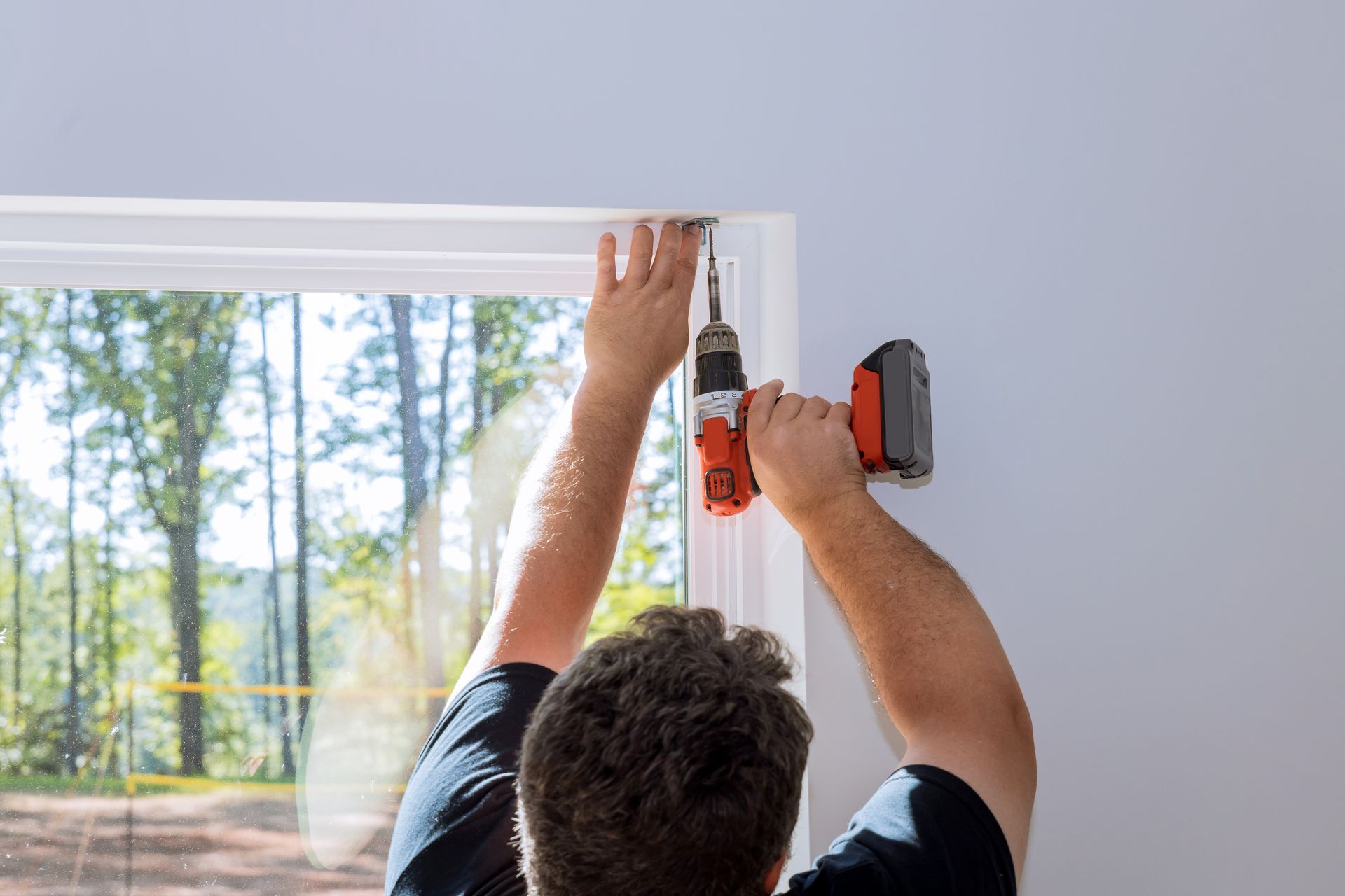 Person drilling a window frame with a cordless drill during home installation work