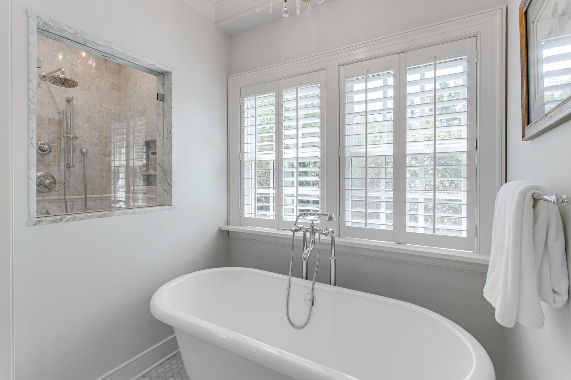 Bright white bathroom with freestanding tub, tiled shower, and window shutters
