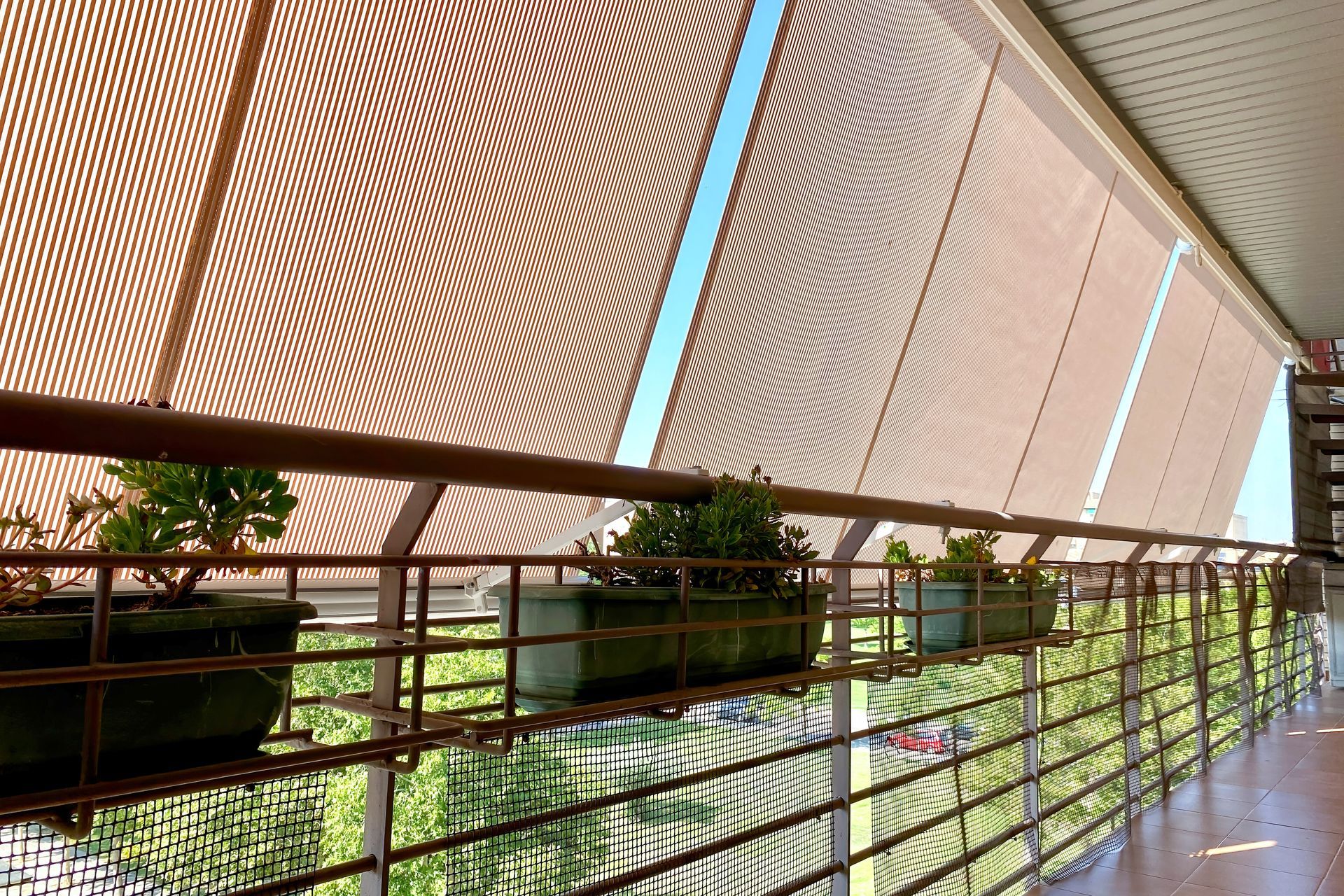 Modern walkway with slanted wood canopy, metal railing, and potted plants in bright sunlight