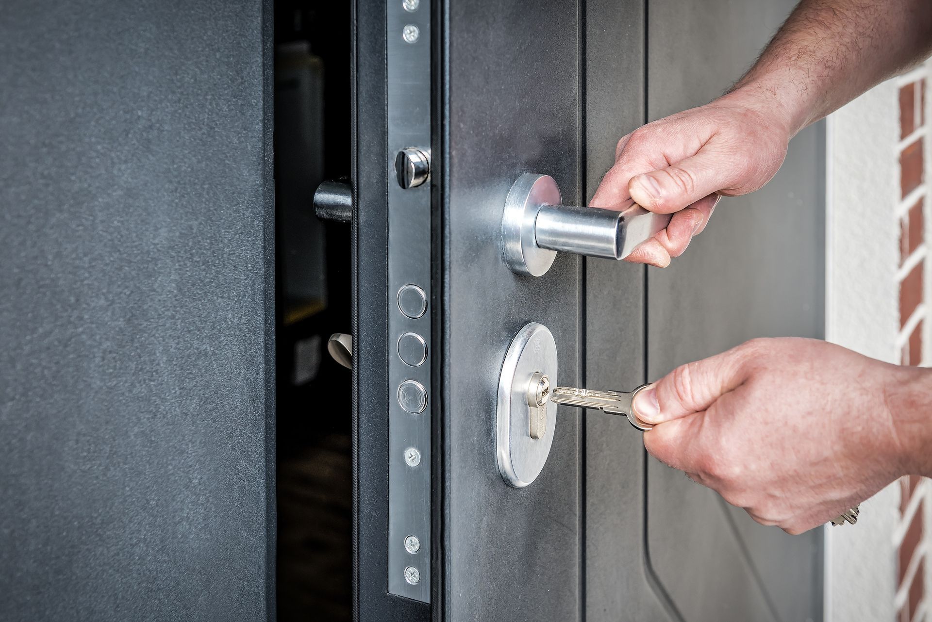Hands using a key and door handle to open a black security door